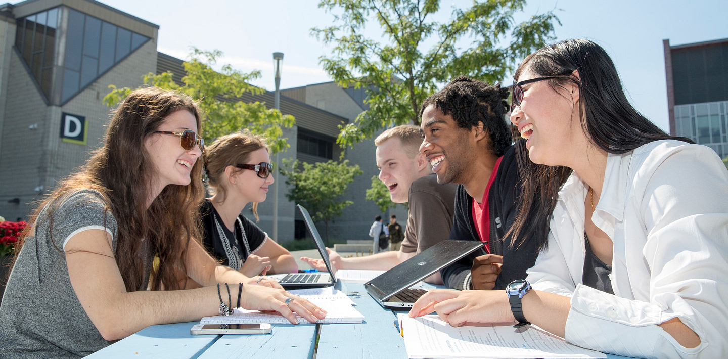 picture of Centennial College students talking and smiling at a picnic table in the Progress Campus courtyard